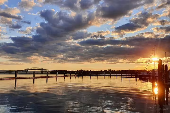 Scenic sunset over Auckland Harbour Bridge with vibrant skies reflecting on calm waters, perfect for photography.