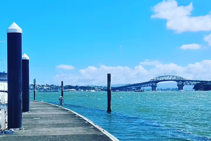 Scenic view of Auckland's iconic Harbour Bridge from a sunny waterfront pier on a clear day.