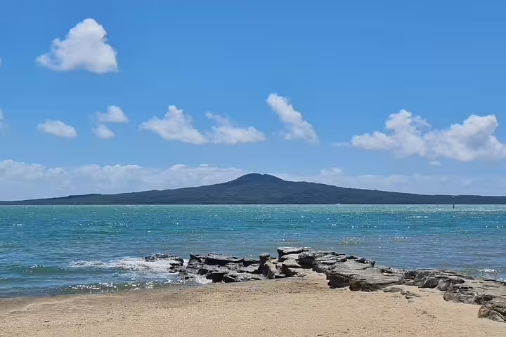 View of Rangitoto Island from a sandy beach on a sunny day, showcasing Auckland's stunning coastal scenery.