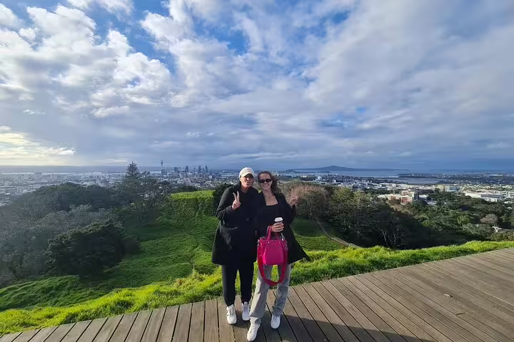 Two friends pose with Auckland's skyline in the background, enjoying a scenic moment on a private day tour.