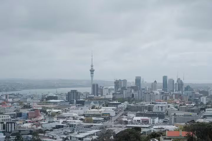 Panoramic view of Auckland skyline with iconic Sky Tower and harbor, showcasing the vibrant cityscape on a cloudy day.