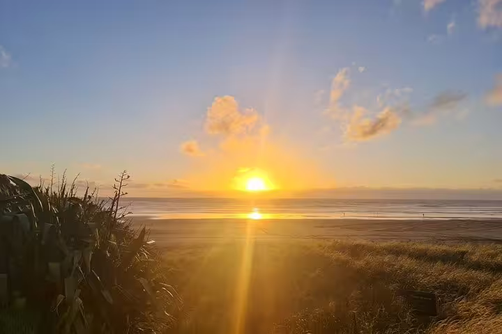 Experience a breathtaking sunset on Auckland's serene beach, ideal for couples on a romantic tour with wine tasting.