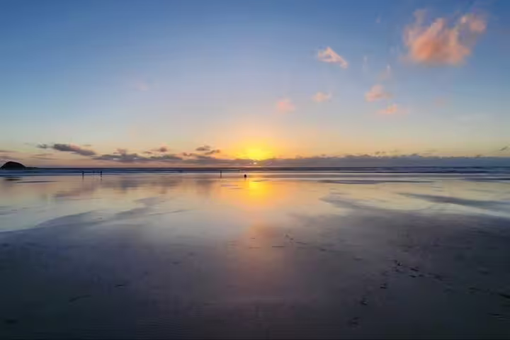 Serene Auckland beach sunset reflecting on calm waters, perfect for a romantic tour with winery and thermal pool.