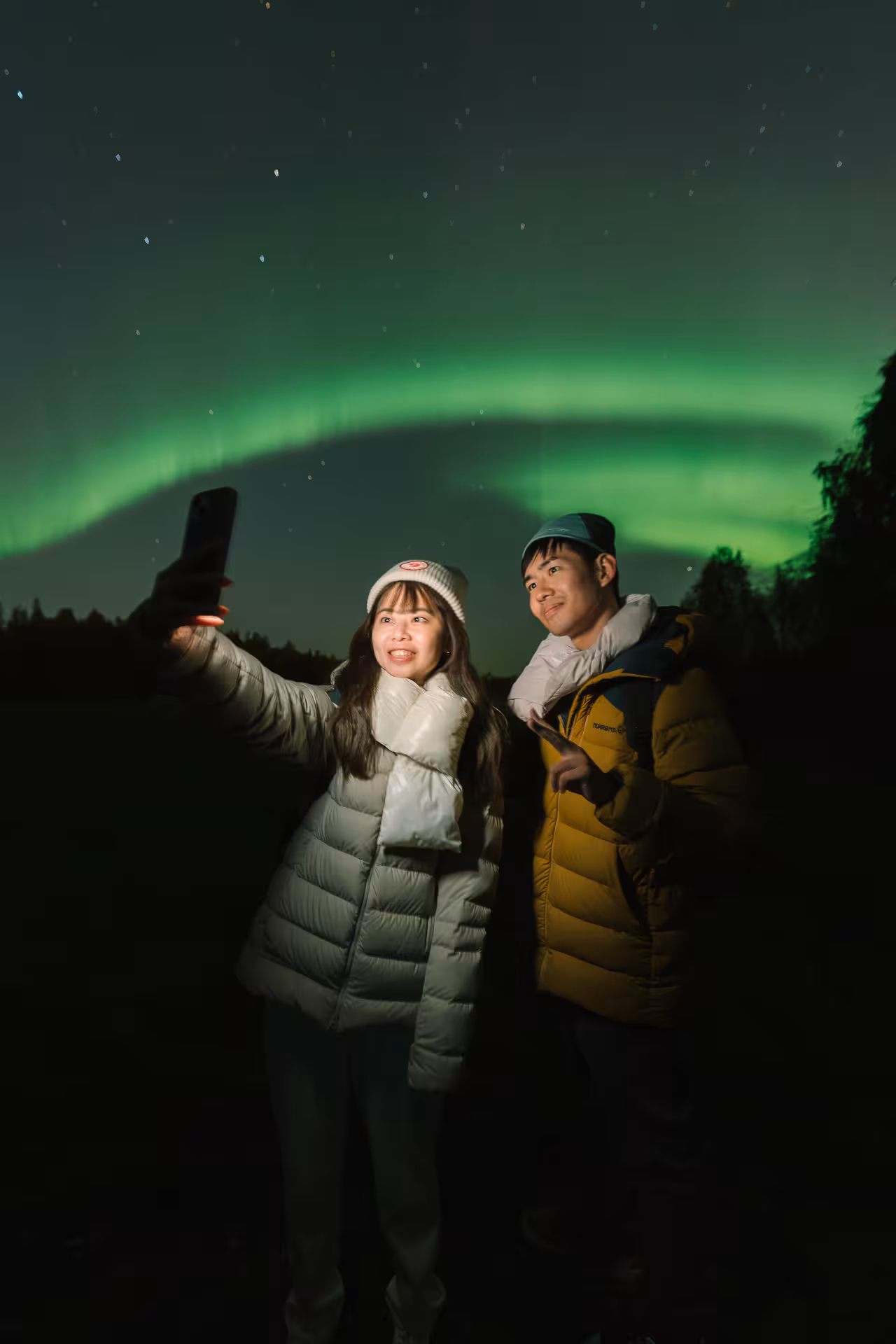 Two people take a selfie beneath the glowing green aurora on an exclusive photography adventure.