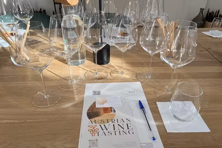 Austrian wine tasting setup with multiple glasses, water, and tasting notes booklet on a wooden table