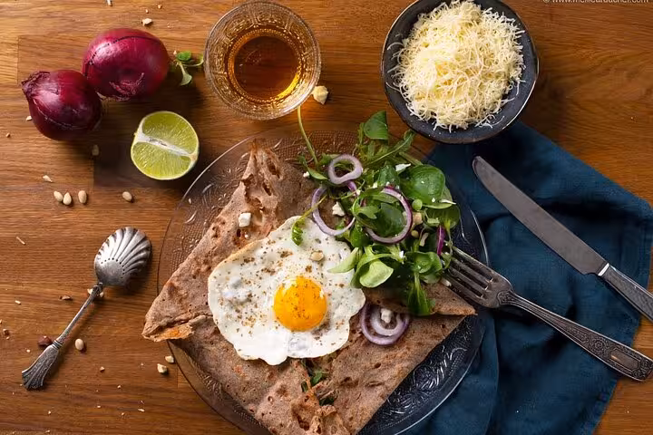 Authentic Parisian galette with fried egg, salad, and grated cheese on a rustic table in Le Marais food tour.
