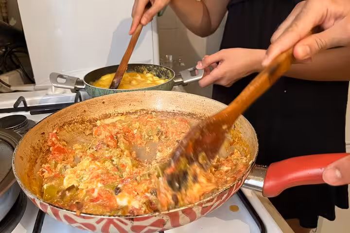 Stirring menemen and creamy eggs in pans during authentic homemade Turkish breakfast cooking with locals