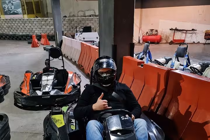 Driver in helmet seated in go-kart at AUTOVROOOM, ready for thrilling karting experience beside safety barriers