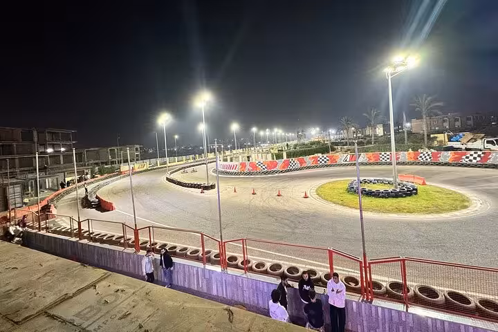 Night view of AUTOVROOOM karting track with floodlights, sharp turns, barriers and spectator area