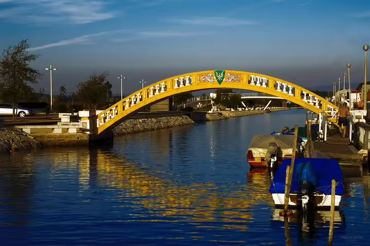 Scenic view of a decorative bridge over Aveiro's canal at sunset, reflecting vibrant colors on the water.