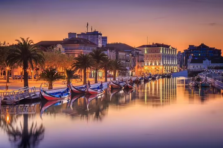 Sunset view of Aveiro's canal with traditional boats and lit-up buildings, ideal for a private Porto-Aveiro tour experience.