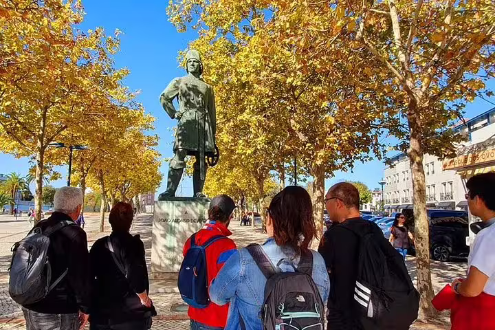 Tourists admire a historic statue in Aveiro, surrounded by golden autumn trees on a sunny day.