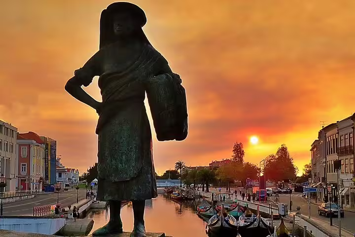 Sunset view of Aveiro canal with iconic statue and traditional moliceiro boats on a private full-day tour from Porto.