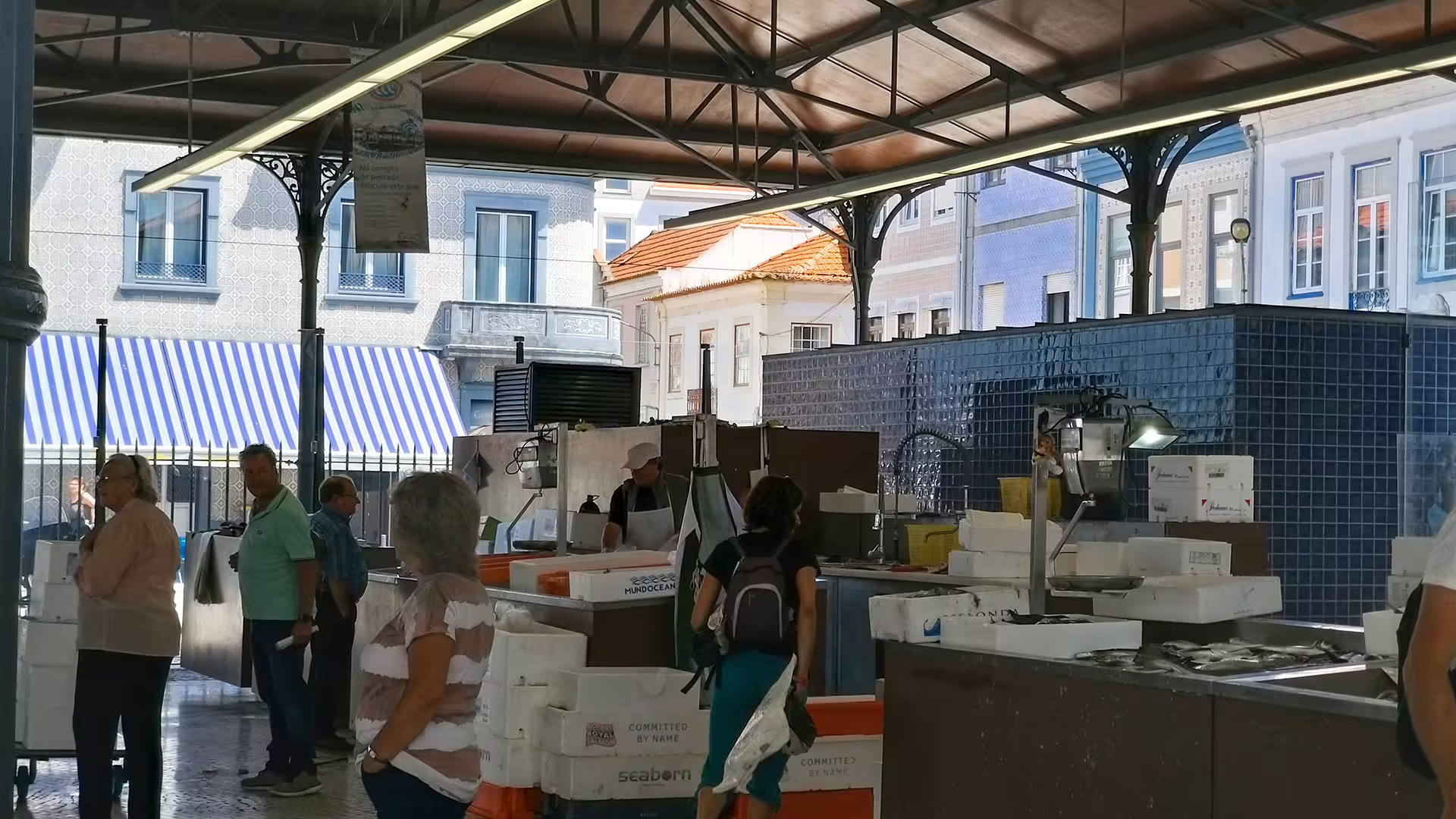 Visitors explore a lively fish market in Aveiro, Portugal, surrounded by vibrant architecture and local striped awnings.