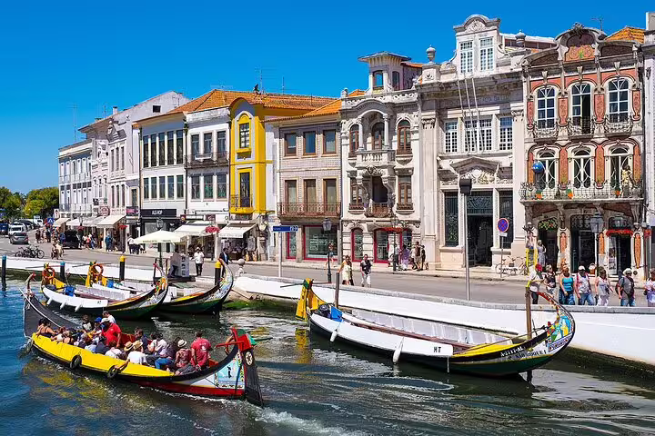 Colorful moliceiro boats glide along the picturesque canals of Aveiro, showcasing the city's historic architecture on a sunny day.