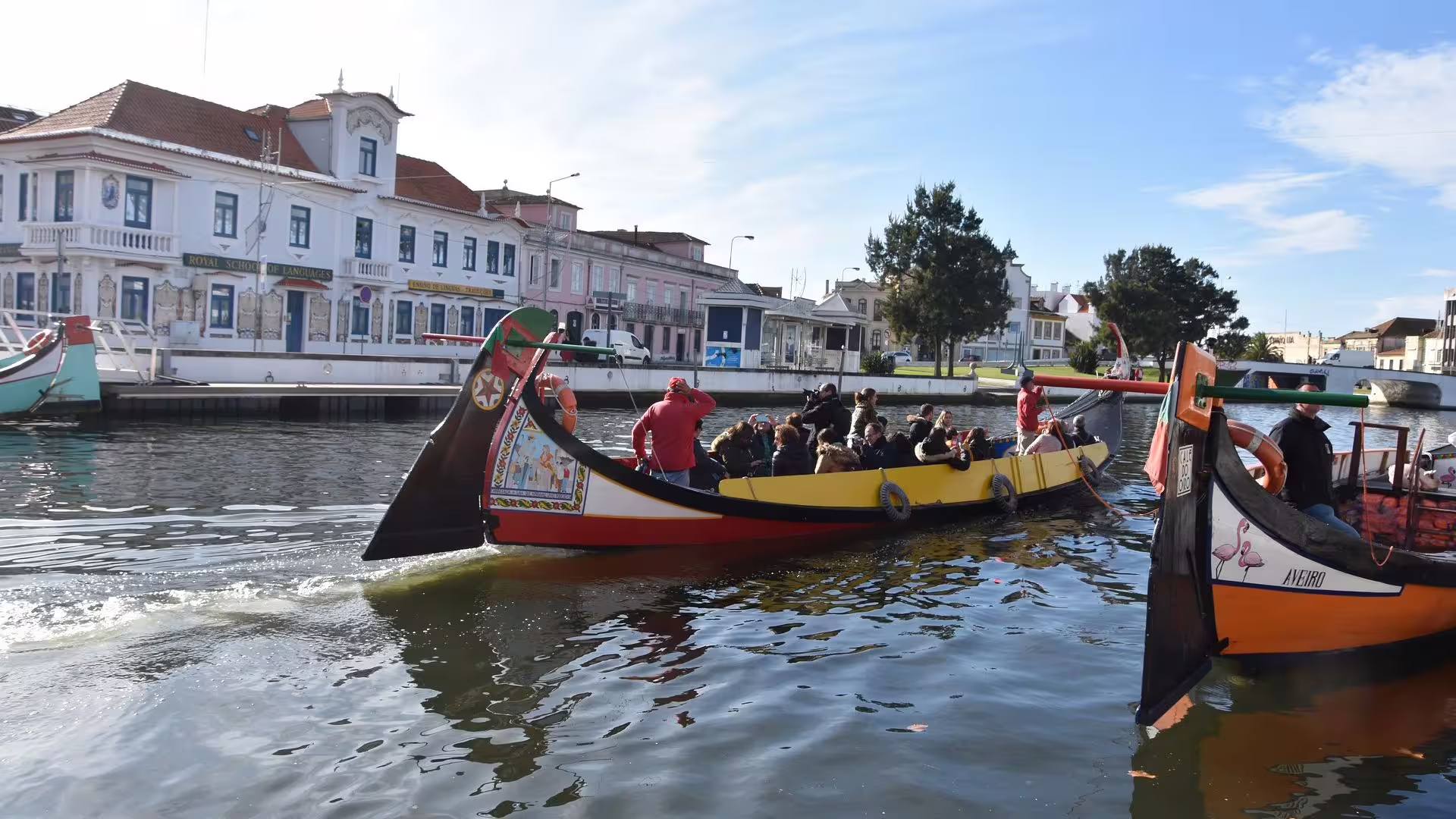 Tourists enjoy a moliceiro boat ride on Aveiro's picturesque canal, surrounded by historic architecture.