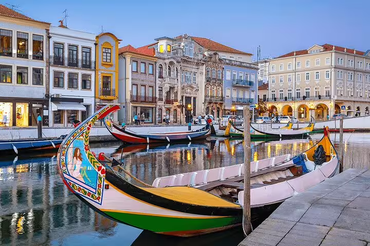 Traditional moliceiro boats float along Aveiro's charming canal, surrounded by colorful historic buildings at dusk.