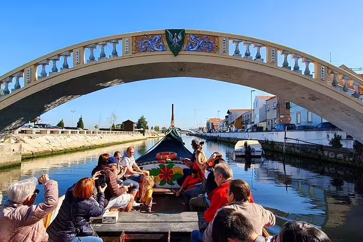 Tourists enjoying a scenic Moliceiro river cruise under a decorative bridge in Aveiro, known as the Venice of Portugal.