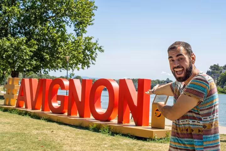 Excited tourist posing with the iconic Avignon sign, showcasing the city's vibrant atmosphere on a sunny day.