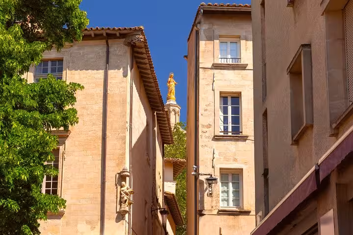 Charming narrow street in Avignon with golden statue visible between rustic buildings, ideal for an intro city walk.