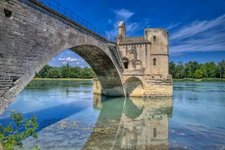 Scenic view of the historic Pont Saint-Bénézet bridge in Avignon reflecting over the Rhône River under a clear blue sky.
