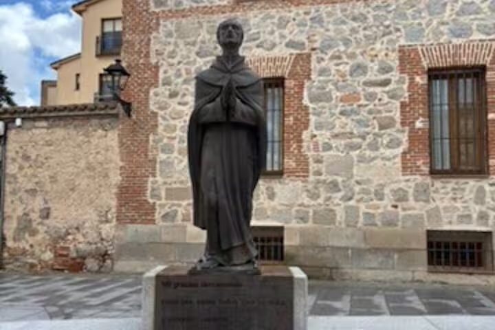 Cloaked monk statue by medieval stone wall in Avila, scenic photo stop on half-day private minivan tour