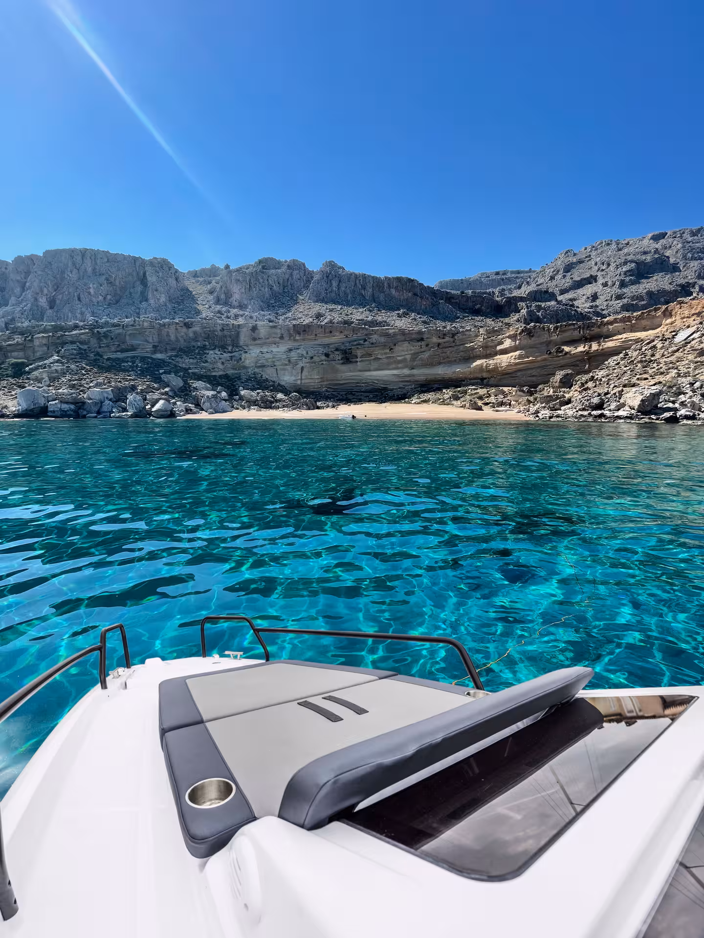 Bow sunpad view on Axopar 25 CT cruising to a secluded cove with emerald waters and limestone cliffs