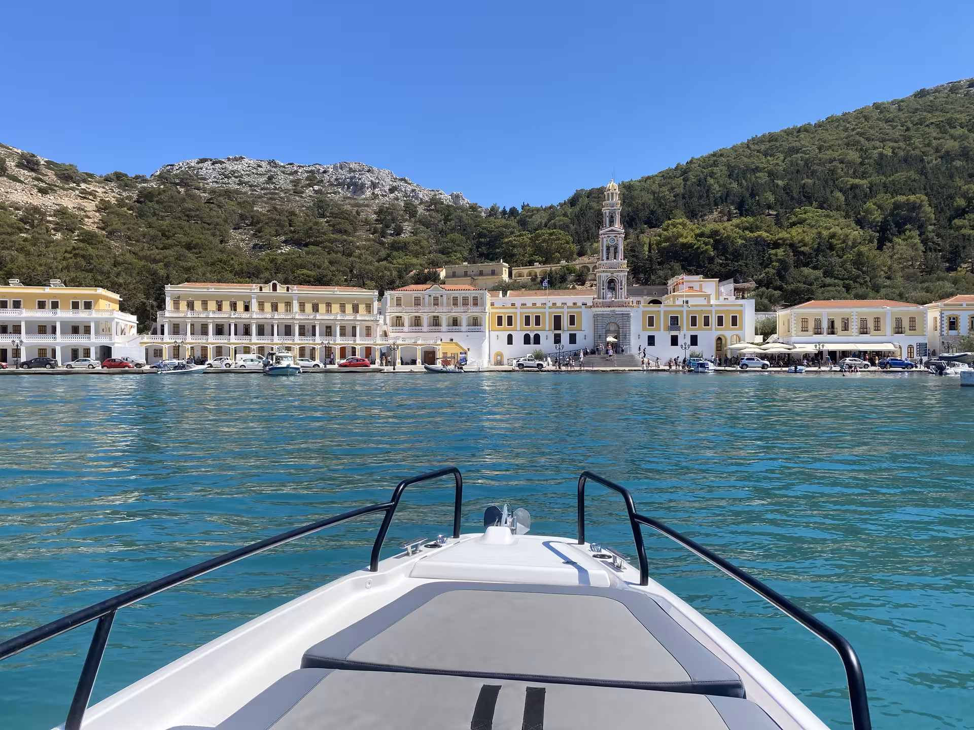Axopar 25 CT bow view arriving at Symi harbor with Panormitis bell tower and neoclassical waterfront