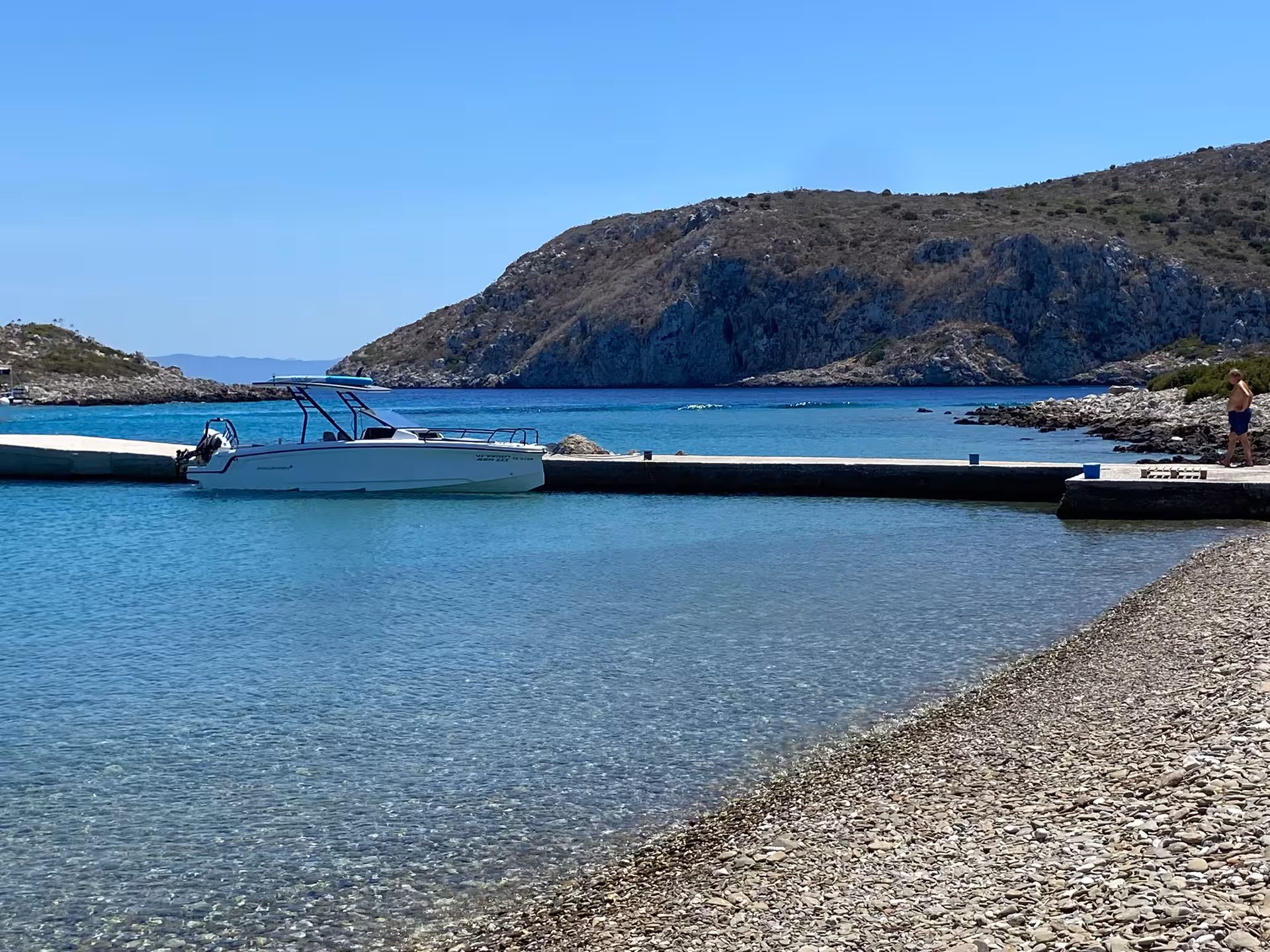 Axopar 25 CT moored by a pebble beach in a turquoise Symi bay, ideal for private island cruise and swim stop