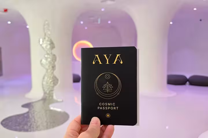 Hand holding Aya Universe cosmic passport in futuristic white interior during private videography tour in Dubai.