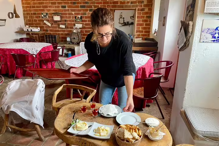 A woman sets up a rustic table with Azeitão cheese and wine, highlighting the authentic experience of a Sesimbra tour.