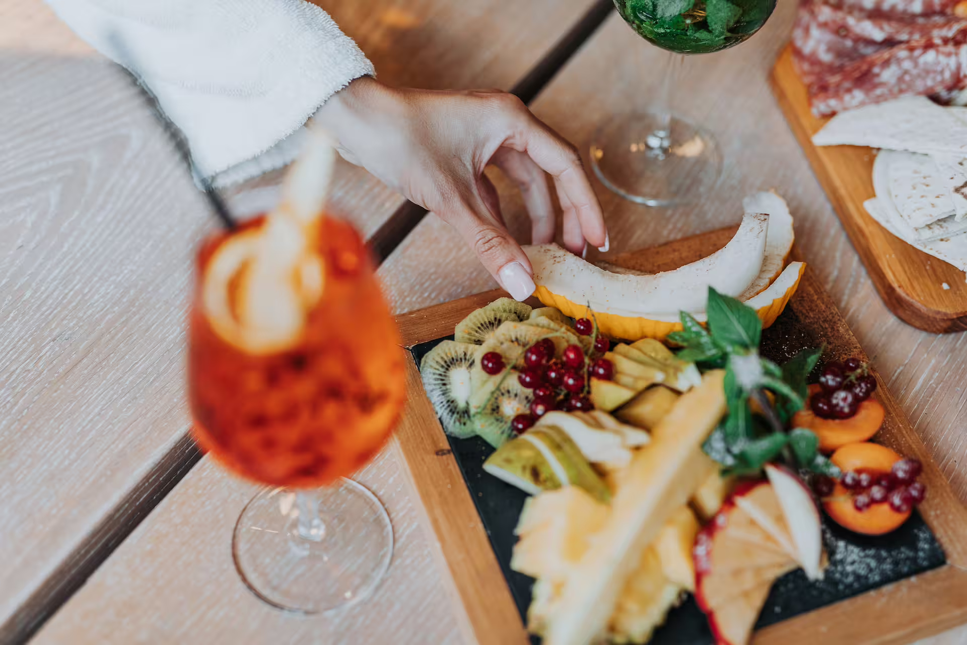 Hand reaching for fresh fruit platter with spritz during Bagno di Romagna thermal pool entry and aperitif