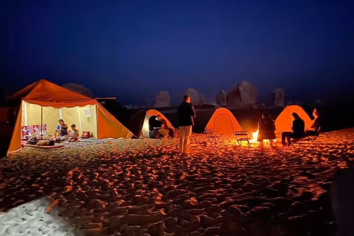 Night desert camp in Bahariya Oasis with glowing tents and campfire, stargazing on a 3-day eco camping tour