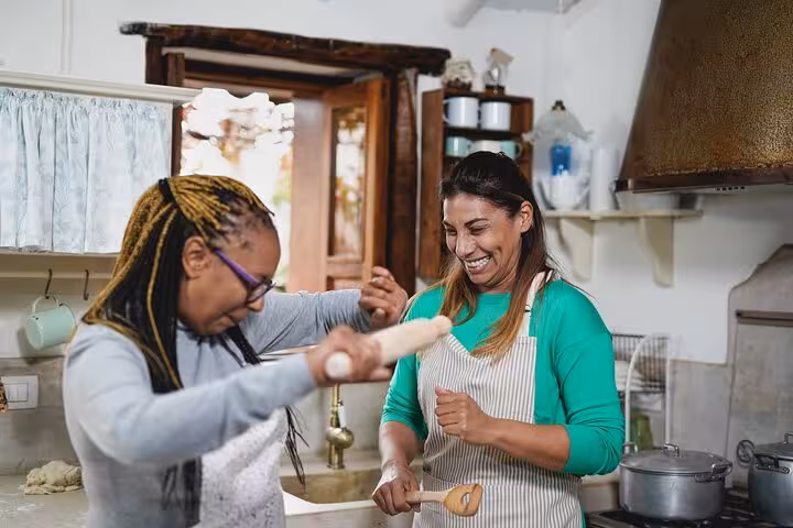 Two women joyfully preparing a dish in a cozy kitchen during a Bahian cooking class in Salvador.