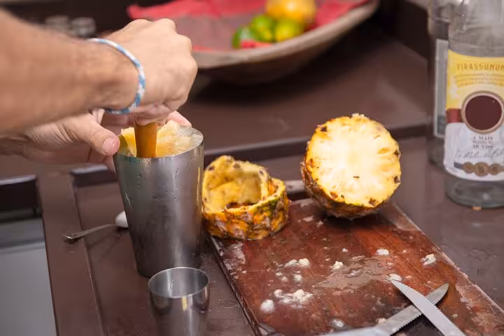 Hands mixing tropical cocktail in a shaker with fresh pineapple during a Bahian cooking class in Salvador.