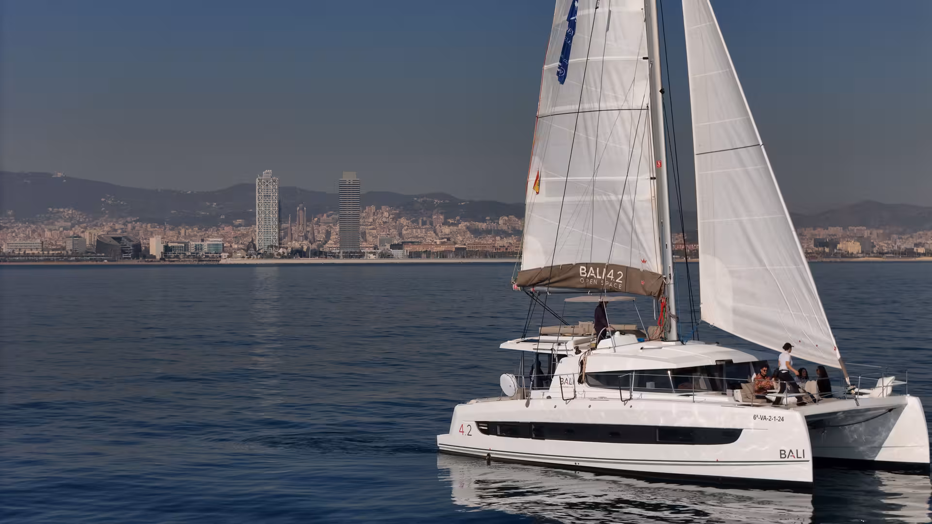 Bali 4.2 luxury catamaran sailing off Barcelona coastline, private 3-hour charter with skyline in background