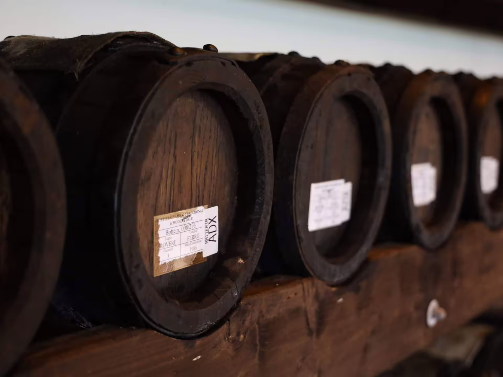 Labeled aging barrels in a Modena acetaia, showcasing traditional balsamic vinegar production and tour
