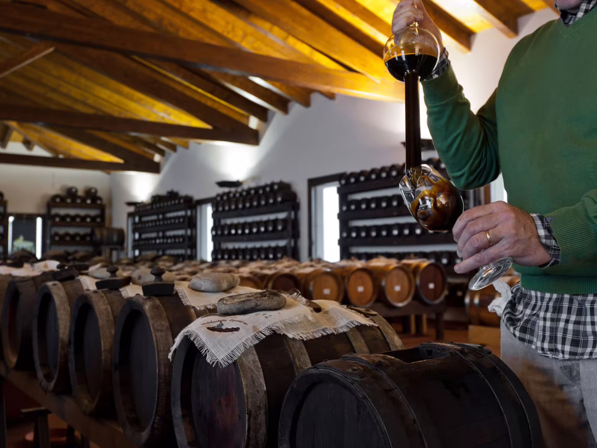 Pouring aged balsamic vinegar in Modena acetaia, surrounded by wooden barrels on production tour and tasting