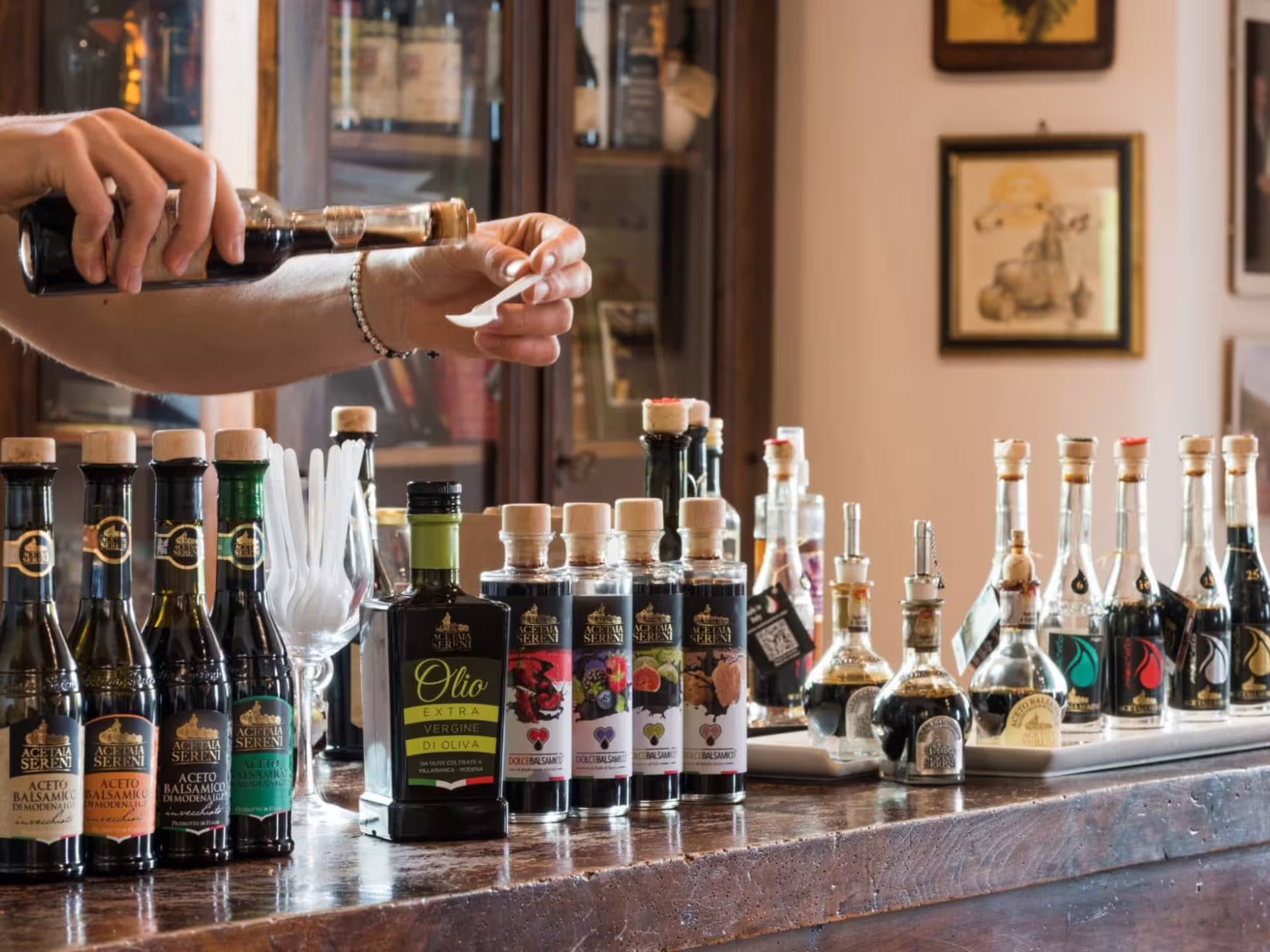 Pouring traditional balsamic vinegar for tasting beside Acetaia bottles during Modena production tour