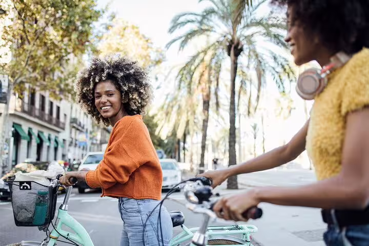 Two people enjoying a sunny Barcelona bike tour with palm trees in the background, perfect for exploring the city and visiting Sagrada Familia.