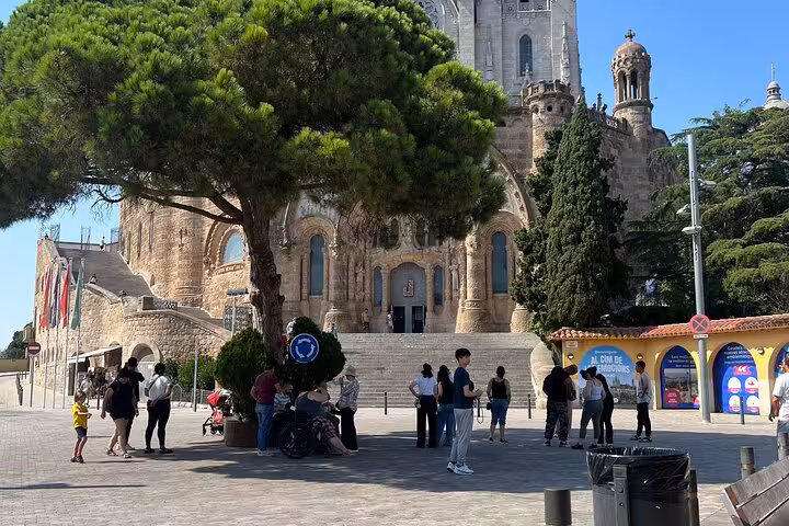 Visitors gather under a shady tree near the entrance of Tibidabo Basilica during the Barcelona city tour.