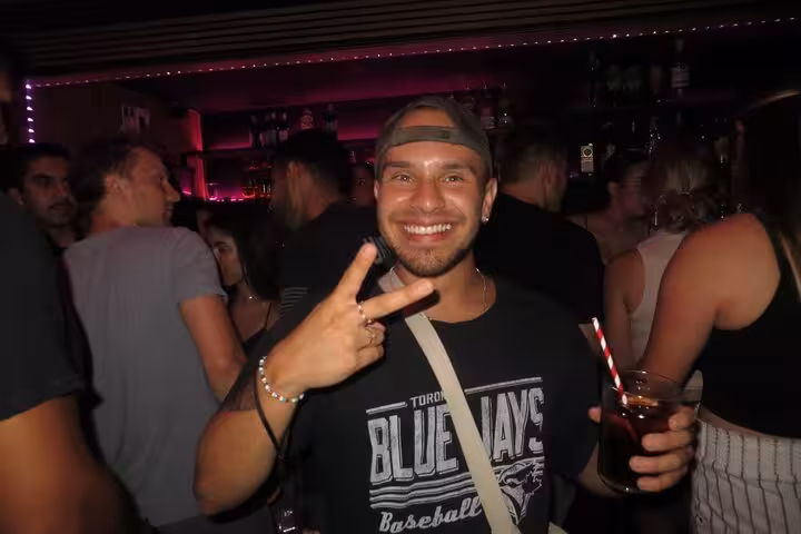 Smiling man in a lively Barcelona club holding a drink, embodying vibrant nightlife with music and socializing.