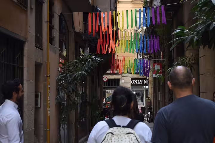 Tourists exploring a colorful, narrow Barcelona street with rainbow decorations during a cultural walking tour.