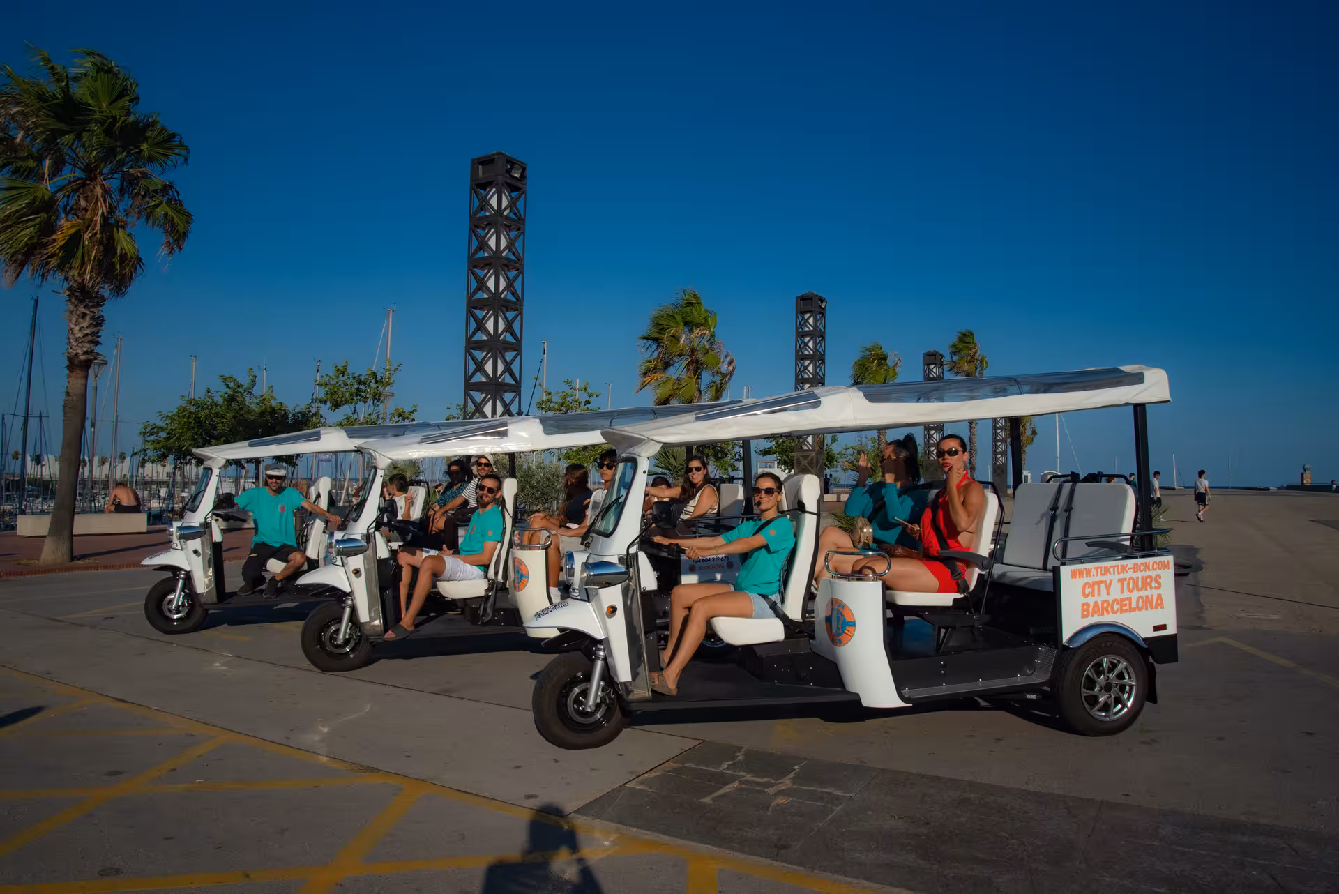 Welcome Tour Barcelona electric tuk tuk fleet by the marina, guided city sightseeing with sea views and palm trees