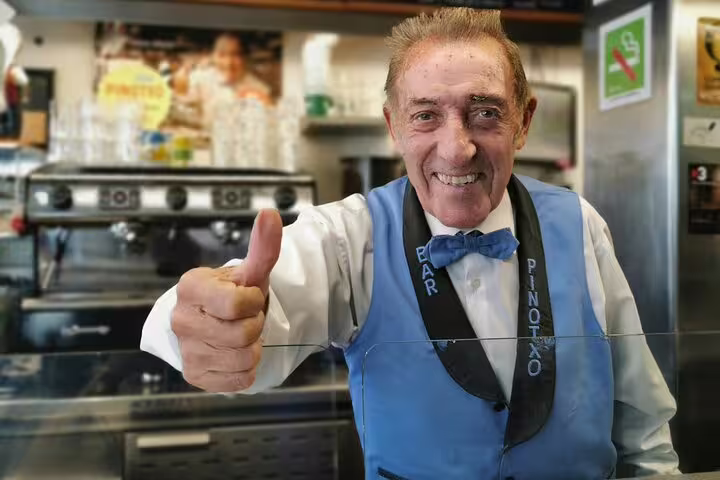 Friendly barista in blue vest gives thumbs up at local café, capturing the vibrant atmosphere of Barcelona's food tour.