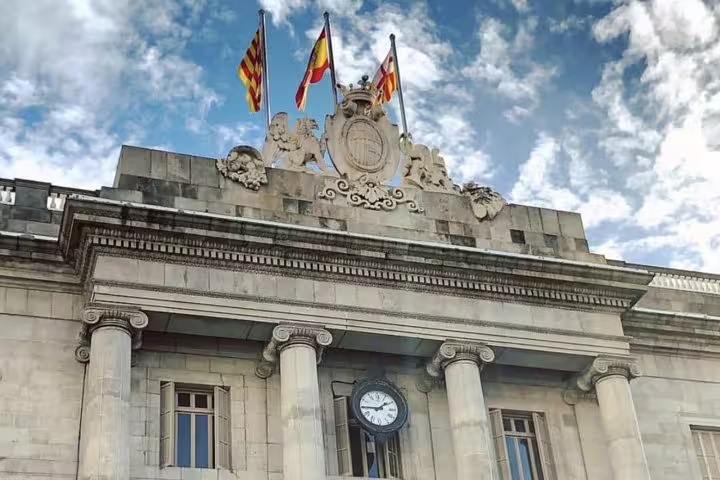 Historic Barcelona building with ornate architecture, flags, and clock, showcasing Catalonia's rich cultural heritage on city tour.