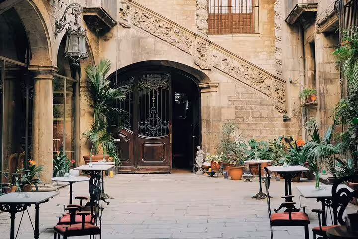 Charming Gothic courtyard with ornate staircase and tables in Barcelona's historic city center.