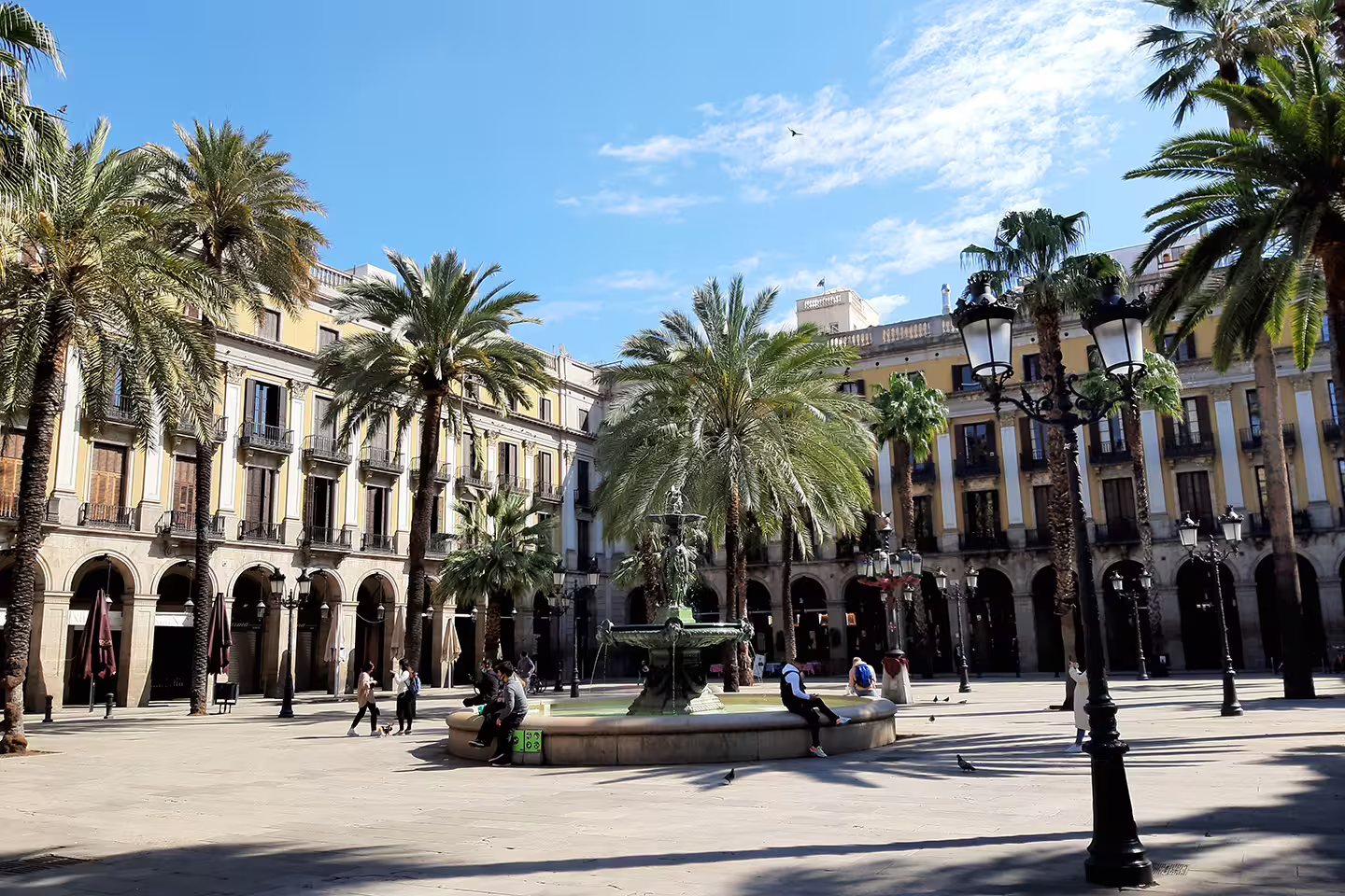 Relax at the picturesque Plaça Reial in Barcelona's Gothic Quarter, featuring palm trees and historic architecture.