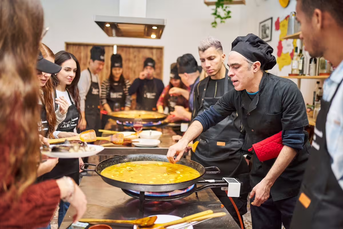 Chef guiding participants in a lively Ultimate Paella Cooking Class, showcasing authentic Spanish culinary techniques in a vibrant kitchen.