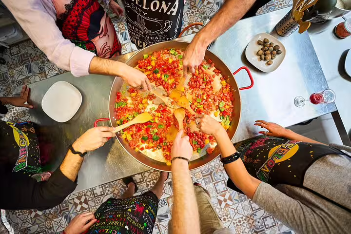 Group of people cooking colorful paella together in a large pan during an interactive culinary class experience.